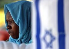 A Sudanese refugee stands, 11 July 2007, behind an Israeli flag at a park near the Israeli Parliament building in Jerusalem, during a rally calling the Israeli government for assistance. (AFP Photo)