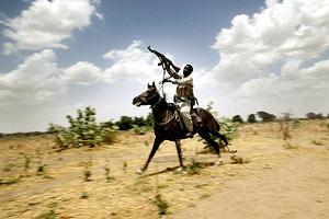 An armed pro-government janjaweed fighter passes by a Sudanese camel herder from one of Darfur's dominant nomad Arab tribes, Rezeigat, at the marketplace in the West Darfur town of Mukjar, Sudan (AP)