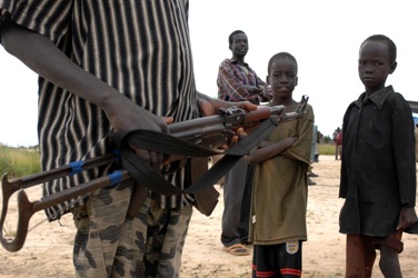 An armed civilian on the airstrip of Dul Padiet standing next to local children (UNMIS- Timothy Mckulka)