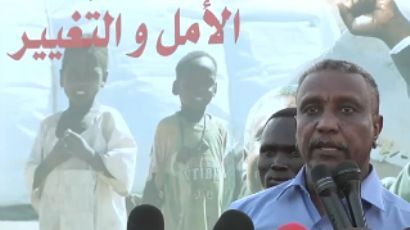 Arman speaking in a meeting while his slogan 