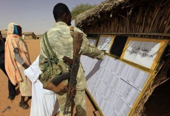 A SLM-Minni Minnawi member helps internally displaced people to find their names on a voters list posted outside a polling station in ZamZam IDP's camp in Al Fasher (Reuters)