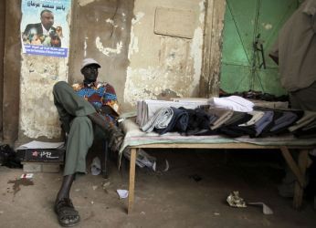 A street vendor sits in front of an election campaign poster of Yasser Arman, the SPLM candidate for the upcoming presidential election in Khartoum March 31, 2010. (AP)