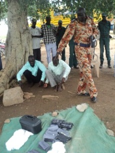 Akot Deng Akot, N. Bahr el Ghazal police commissioner (standing) displays some of the materials allegedly used by the two men (seated) to make fake US dollars, August 25, 2011 (ST)