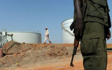 A Southern Sudanese soldier (R) stands next to crude oil reservoir tanks while a foreign Greater Nile Petroleum Operating Company (NPOC) oil worker walks by at a field processing facility in Unity State on November 10, 2010. (Getty)