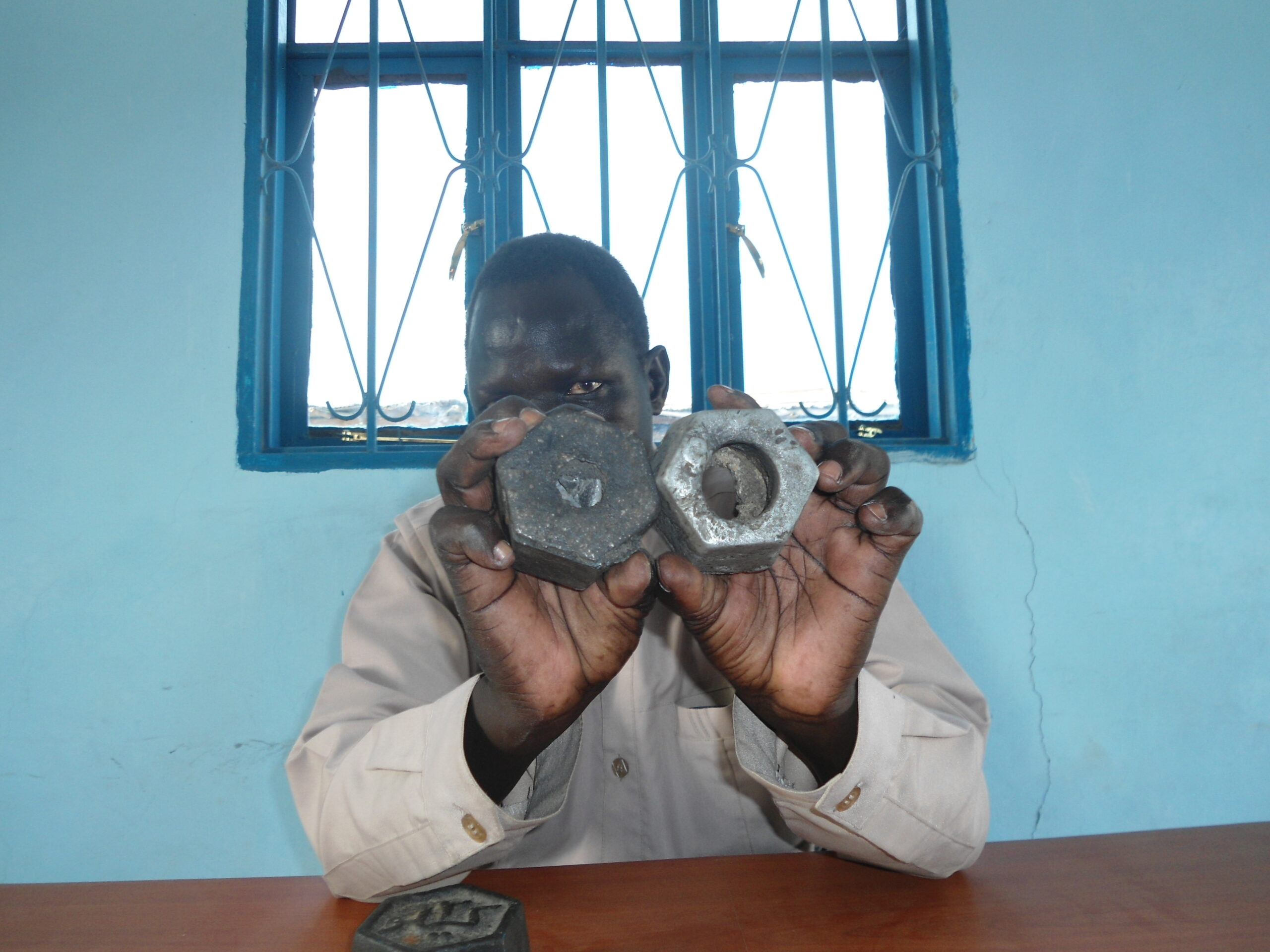 Dircetor of Grades and Standard Measures, Anyuon Deng, showing the right weighing stone in his left hand and a faulty weighing stone in his right hand in his office in Bor Marol Market, 27 April 2012 (ST)