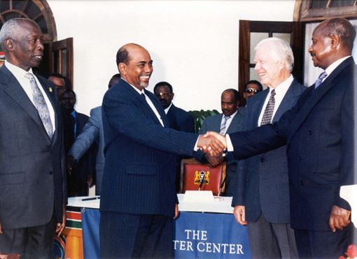 Former U.S. President Jimmy Carter mediated a peace accord between Sudan and Uganda on Dec. 8, 1999, in which the two countries agreed to take steps to restore diplomatic relations and promote peace in the region.  Sudan President Omar Al-Bashir (left) shakes the hand of Uganda President Yoweri Museveni. Kenya President Daniel arap Moi and President Carter witnessed the signing. (Photo: Carter Center)