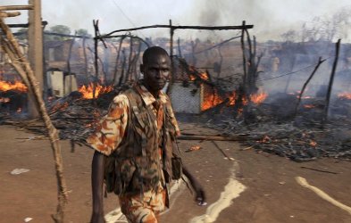 A policeman walks past the smouldering remains of a market in Rubkona near Bentiu in South Sudan Monday, April 23, 2012. (AP Photo/Michael Onyiego)