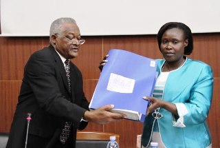 UNEB Chairman, Fagil Mandy (L) hands over the PLE result to Uganda's education minister, Jessica Alupo (New Vision)