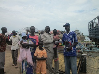 James Jok, the Relief and Rehabilitation Commission (RRC) coordinator, carrying a returnee child, while standing between the father and mother in Bor, June 28, 2013 (ST)