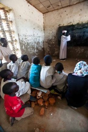 Students of Bakht Alrida Primary School in the IDPs camp in Forobaranga, West Darfur, listen to the headmaster Abdulrahman Idris on 14 September 2013. The center, with 4 teachers and 338 students, has many deficiencies and infrastructural problems. All seven classrooms don't have furniture (desks and chairs for the students) or it's seriously damaged. The local community claim for an urgent rehabilitation. Photo by Albert González Farran, UNAMID).