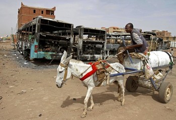 FILE - In this Thursday, Sept. 26, 2013 file photo, a man on a donkey cart passes burned buses following rioting and unrest in Khartoum (AP Photo/Abd Raouf)