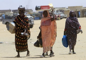 FILE - Three women carry bags as they walk through the Abushuk refugee camp in the North Darfur state capital of EL Fasher on June 17, 2013 (ASHRAF SHAZLY/AFP/Getty Images)