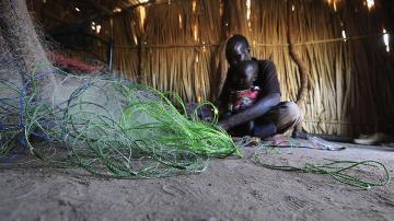 A South Sudanese man repairs fishing nets inside a shelter in al-Ghanaa village in the Jableen locality in Sudan's White Nile state on 17 January 2014 (Photo: Reuters/Mohamed Nureldin Abdallah)