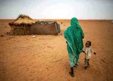 A child walks with her mother to their shelter at the Zam Zam camp for displaced people in North Darfur on 11 June 2014 (Photo: Albert Gonzalez Farran/AFP/Getty Images)