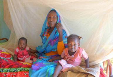 A Sudanese woman sits with her two children under a mosquitor bednet at the Draij camp outside South Darfur capital Nyala (Photo: UNICEF/Simonsen)