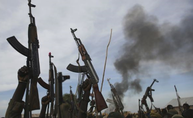 Rebel fighters hold their weapons in the air as they walk in front of a bushfire in rebel-controlled territory in South Sudan's Upper Nile state on 13 February 2014 (Photo: Reuters)