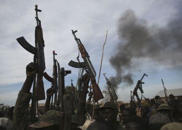 South Sudanese rebel fighters hold up their rifles as they walk in front of a bushfire in rebel-controlled territory in Upper Nile state on 13 February 2014 (Photo: Reuters)