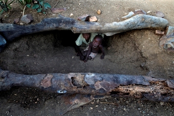 Nasra Sulliman, 55, with her grandchild inside the bomb shelter (foxhole) built just outside their home in Tingal village, in Southern Kordofan, Sudan (HRW/Giovanni Diffidenti)