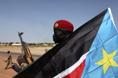 An SPLA soldier is pictured behind a South Sudan flag as he sits on the back of a pick-up truck in Bentiu, Unity state January 12, 2014. (Photo Reuters/Andreea Campeanu)