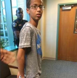 In this Sept. 14, 2015 photo provided by Eyman Mohamed, her brother Ahmed Mohamed stands in handcuffs at Irving police department in Irving, Texas (Eyman Mohamed via AP)