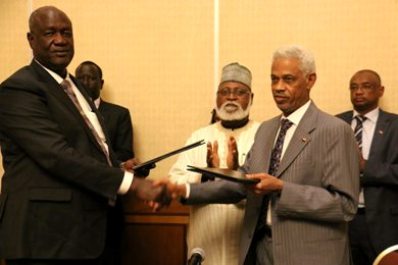 South Sudan's defence minister Kuol Manyang Juuk shakes hands with his Sudanese counterpart Mohamed Ahmed Ibn Ouf while AUHIP member Abdulsalam Abubakar applauds,  after the signing of an agreement to operationalize the buffer zone between the two countries on 14 October 2015 (Courtesy photo by the AUHIP).