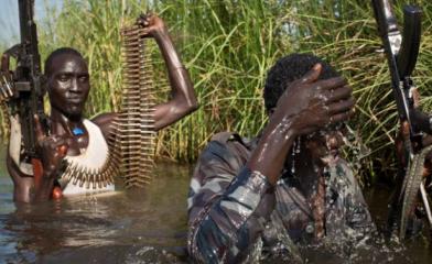 Rebel fighters protect civilians from the Nuer ethnic group (not seen) walk through flooded areas to reach a camp in UNMISS base in Bentiu, Sept. 20, 2014 (Photo AP/Matthew Abbott)