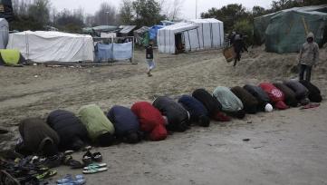 In this Friday, Nov. 6, 2015 photo, muslim migrants attend Friday prayers outside a makeshift mosque at the migrant camp near Calais, northern France. Muslims hold Friday prayers in a half-dozen tents catering to Sunni and Shiite Arabic speakers, Iranian and Afghan speakers of Persian and Pashto, Syrian Kurds, and Sudanese in both Arabic and tribal tongues. (AP Photo/Markus Schreiber)