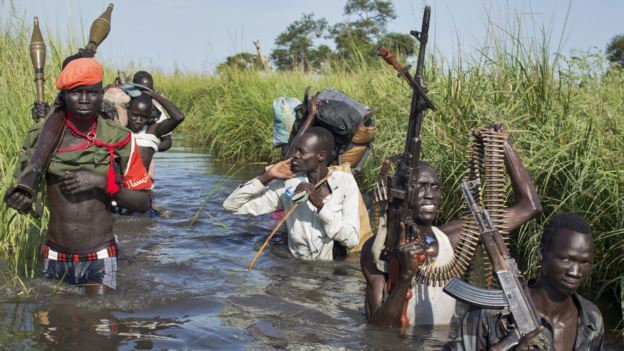 Rebels protect civilians from the Nuer ethnic group (not seen) walking through flooded areas to reach a camp in UNMISS base in Bentiu, Sept. 20, 2014 (Photo AP/Matthew Abbott)
