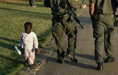 A Sudanese refugee child walks past Israeli Border Police officers in the Rose Garden, just outside Israel’s parliament, in Jerusalem, Sunday, July 8, 2007. (AP)