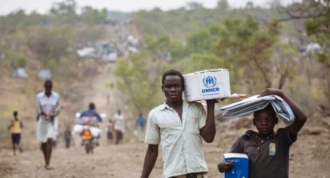 South Sudanese refugees carrying Core Relief Items walk down a road in Bidibidi refugee settlement, Yumbe District, Northern Region, Uganda. (UNHCR/David Azia)