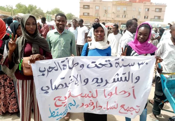 A group of Darfur women outside army garrison in El Fasher hold a banner saying 