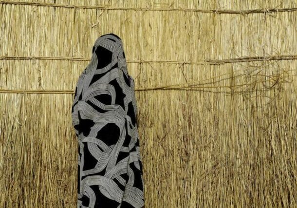 A Misseriya woman stands in front of a thatched shelter