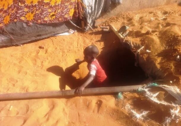 A child climbs out of an underground trench in Abu Shouk camp.