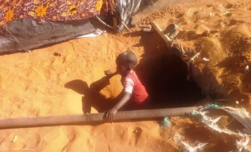 A child climbs out of an underground trench in Abu Shouk camp.