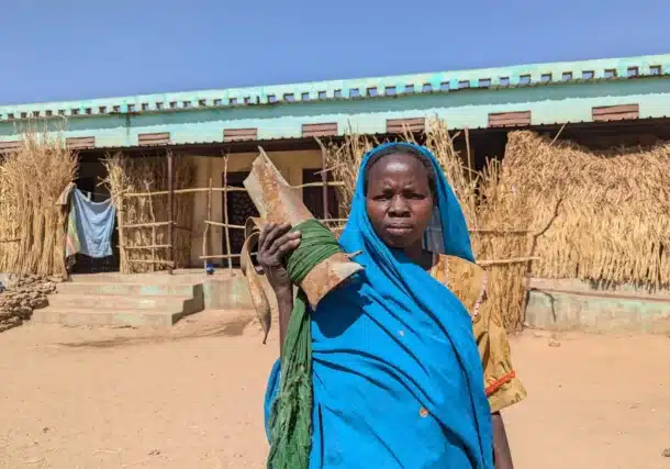 A woman carries remnants of ammunition that hit her house and destroyed it before she moved to live in Al Hamidiya camp in Central Darfur, Sudan.. January 2025.