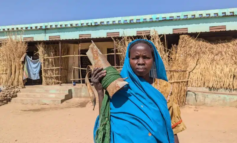 A woman carries remnants of ammunition that hit her house and destroyed it before she moved to live in Al Hamidiya camp in Central Darfur, Sudan.. January 2025.