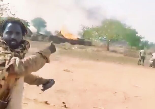 A RSF fighter points towards a burning Sudanese army camp in Um Dehilib, South Kordofan, declaring the area under RSF control, on June 7, 2025.