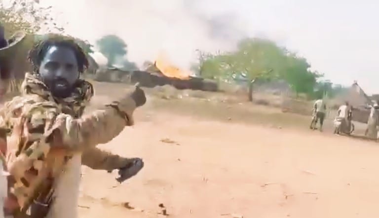 A RSF fighter points towards a burning Sudanese army camp in Um Dehilib, South Kordofan, declaring the area under RSF control, on June 7, 2025.