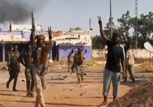 RSF fighters flash victory signs outside the army's 6th Infantry Division headquarters in El Fasher on October 26, 2025.