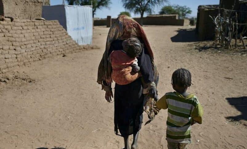 A mother walks with her children to their shelter at an IDP camp in North Darfur in March 2025, UNICEF photo