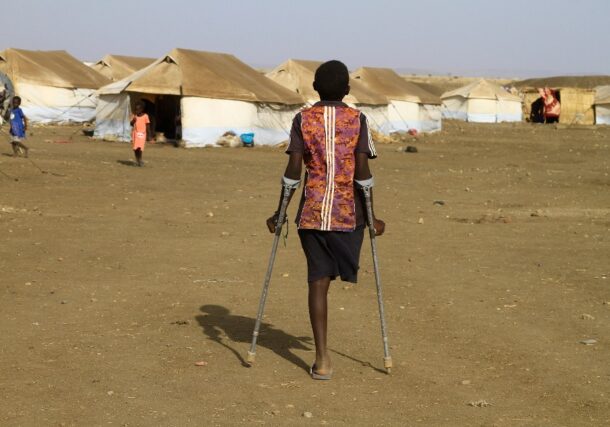 A child walks with the aid of crutches through a displacement camp in eastern Sudan.