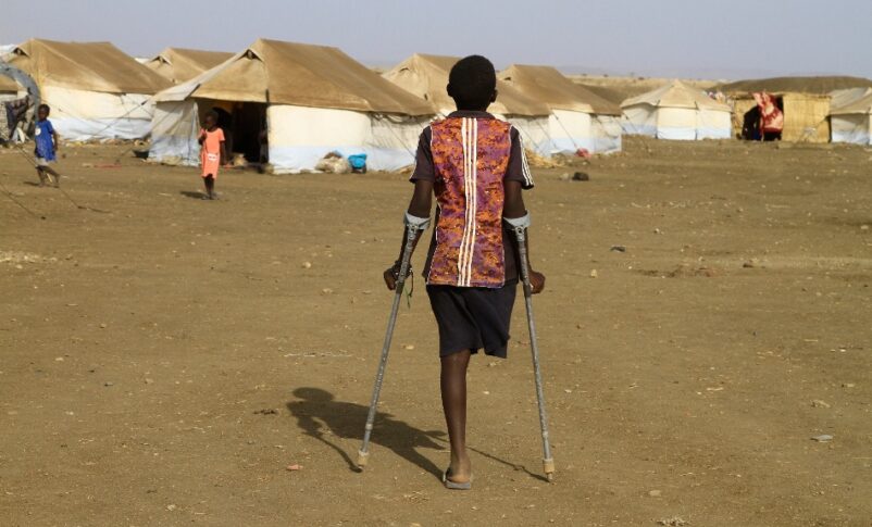 A child walks with the aid of crutches through a displacement camp in eastern Sudan.