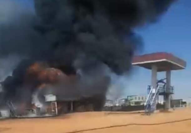 A massive plume of black smoke and bright orange flames rising behind a building following a drone attack in Kenana, While Nile state on May 3, 2026