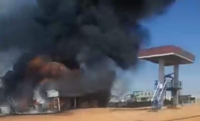 A massive plume of black smoke and bright orange flames rising behind a building following a drone attack in Kenana, While Nile state on May 3, 2026
