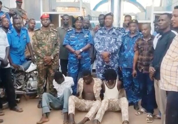 Sudanese police officers and security personnel standing over three suspected gang members sitting on the ground, arrest by Jebel Aulia police in southern Khartoum on July 17, 2026.