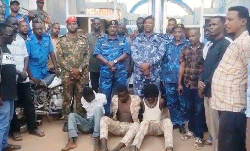 Sudanese police officers and security personnel standing over three suspected gang members sitting on the ground, arrest by Jebel Aulia police in southern Khartoum on July 17, 2026.
