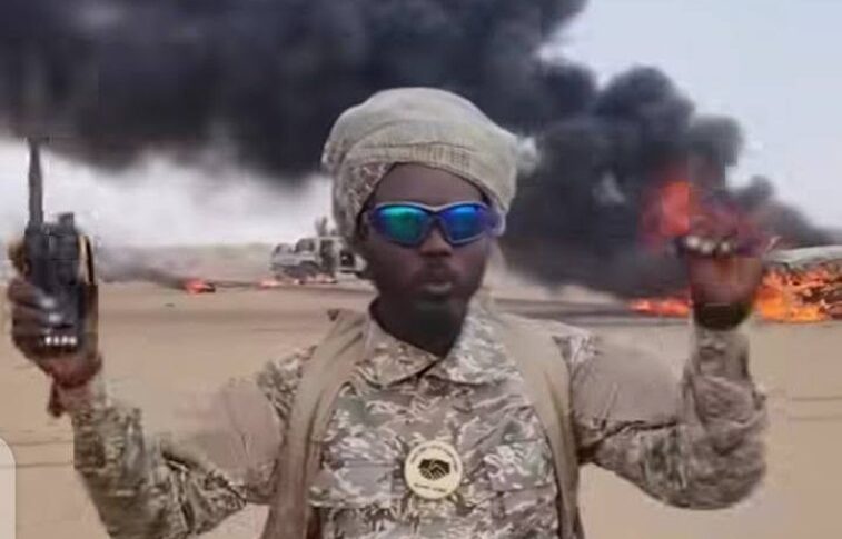 A Joint Force fighter holds a radio in front of burning vehicles following clashes in Sodari, North Kordofan, September 17, 2026.